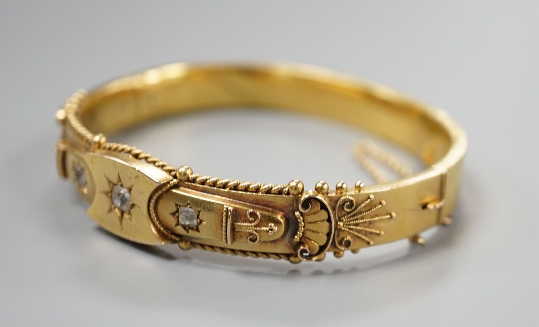 An Edwardian 15ct gold and three stone diamond set hinged bangle, interior diameter 57mm, gross weight 15.8 grams.